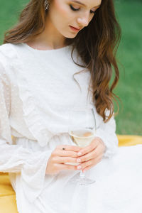 A glass of white wine or champagne in the hands of a young woman in a white dress. the girl looks