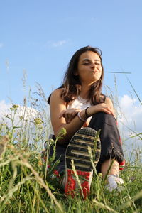 Young woman sitting on field against sky