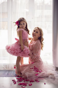 Mom and daughter baby in pink dresses sitting on the floor of the house, background of the window