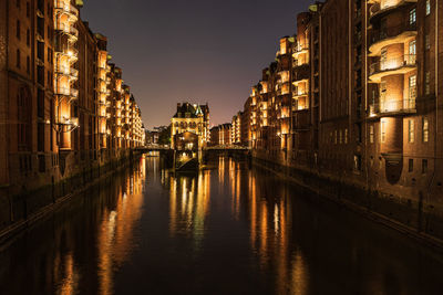 Canal amidst buildings in city at night