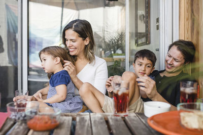 Happy parents sitting with children at table against glass door