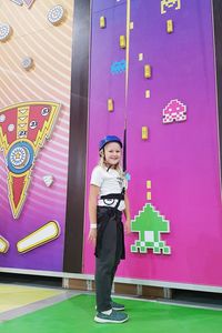 Full length of a smiling girl standing against pink wall