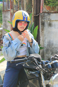 Young woman wearing helmet while sitting on motorcycle against wall