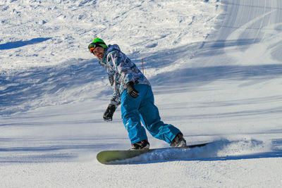 A handsome young man slides down a ski slope on a snowboard. snow flies out from under his board