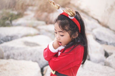 High angle view of girl wearing red dress and headband with mouth open standing on rocks