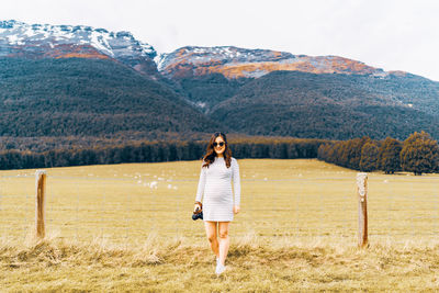Full length of woman standing on grass against mountains and sky