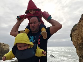 Playful father with children at beach against cloudy sky