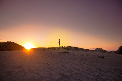 Silhouette man standing on sand against sky during sunset