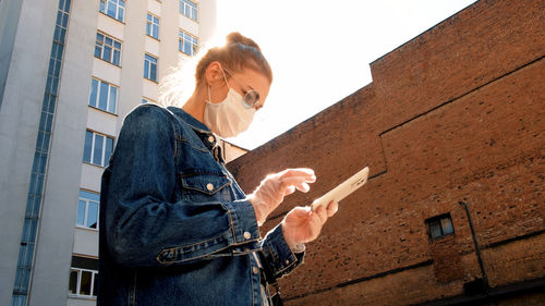 Low angle view of woman using phone while standing on building