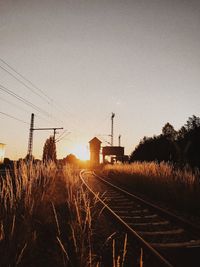 Railroad tracks on field against sky during sunset