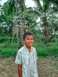 Portrait of young boy standing against trees