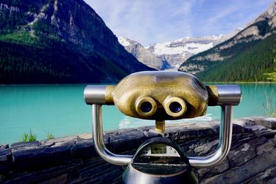 Close-up of coin-operated binoculars by lake against mountains