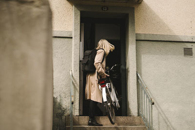 Full length of businesswoman entering building with electric bicycle