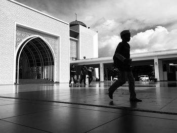 Rear view of man walking by building against sky