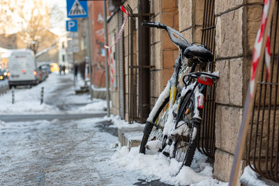 A bicycle covered with ice and icicles on the wall of the building on the sidewalk