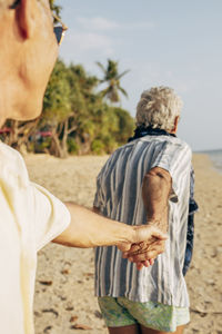 Elderly gay couple holding hands and walking on beach at sunny day