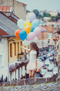 Woman holding balloons with umbrella standing in city