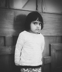 Portrait of cute girl standing against wooden wall