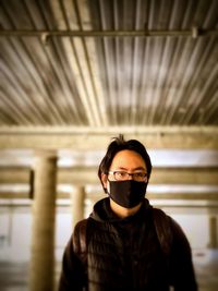 Portrait of young man in face mask standing against ceiling and pillars.