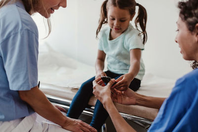 Healthcare worker showing glaucometer to girl by doctor in clinic