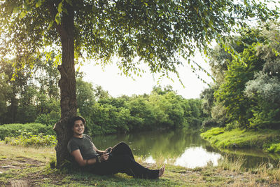 Young woman sitting by lake against trees