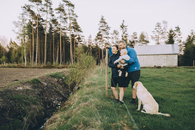 Parents with son and pet dog standing in farm during sunset