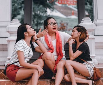 Full length of happy friends sitting outdoors