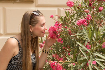 Young woman smelling pink flowers blooming against wall