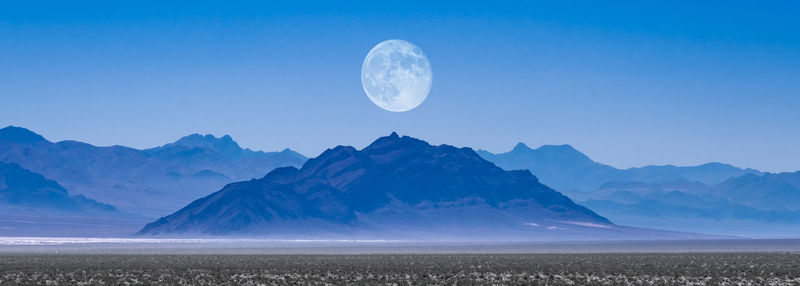 Scenic view of mountains against clear blue sky with a rising moon