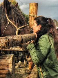 Side view of woman standing by horse at ranch