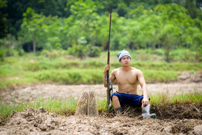 Full length of shirtless man sitting on land
