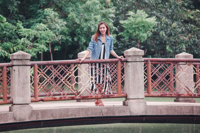 Portrait of smiling young woman standing on footbridge