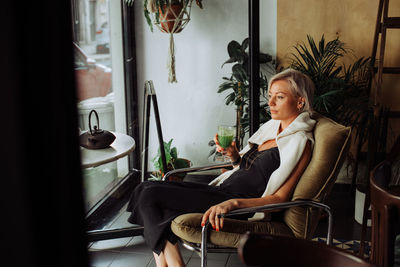 Middle age woman sitting at table in cafe holding green smoothie