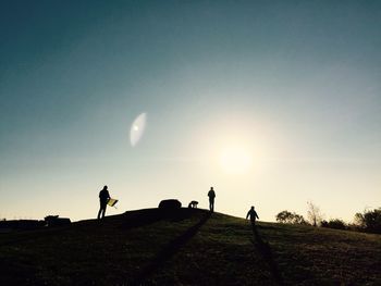 People standing on grassy field against sky at sunset