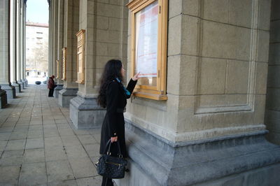 Young woman reading notice on pillar