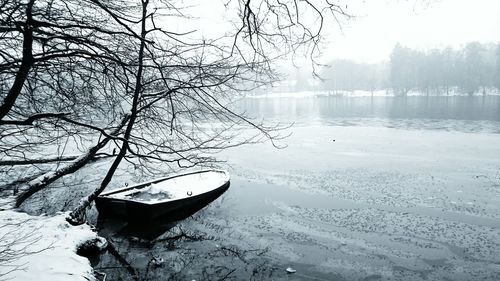 Frozen boat moored in river by tree during winter