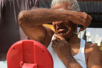 Close-up of senior man shaving while sitting outdoors