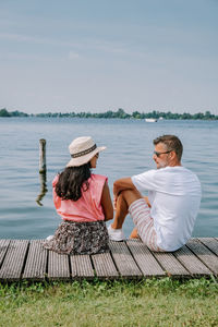 Rear view of couple sitting on shore against sky