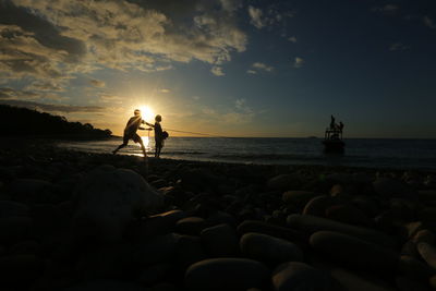 Silhouette people standing on beach against sky during sunset