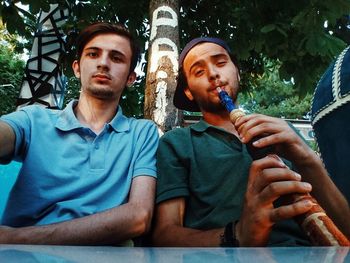 Low angle portrait of male friends sitting at table against tree