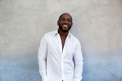 Handsome cheerful african american man in white shirt standing with grey blue textured wall