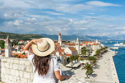 Rear view of woman standing on city walls looking at idyllic seaside town of trogir, croatia