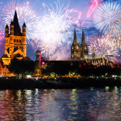 Firework display over river with illuminated buildings in background