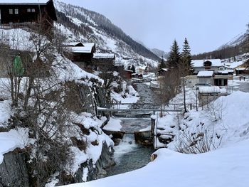 Snow covered houses by trees and mountains during winter