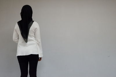 Rear view of woman in hijab standing against gray wall