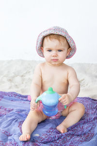 Little baby girl sitting on plaid at beach and holding bottle with water in hands.