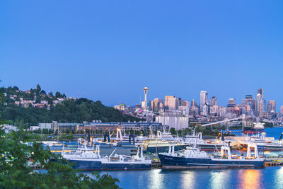 Boats moored in river by buildings against clear blue sky