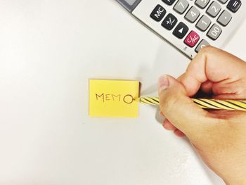 Cropped hand writing memo text on adhesive note at table in office