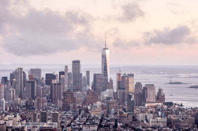 One world trade center in city by river against cloudy sky during sunset