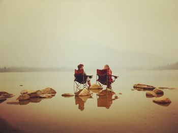 People on rocks by lake against sky